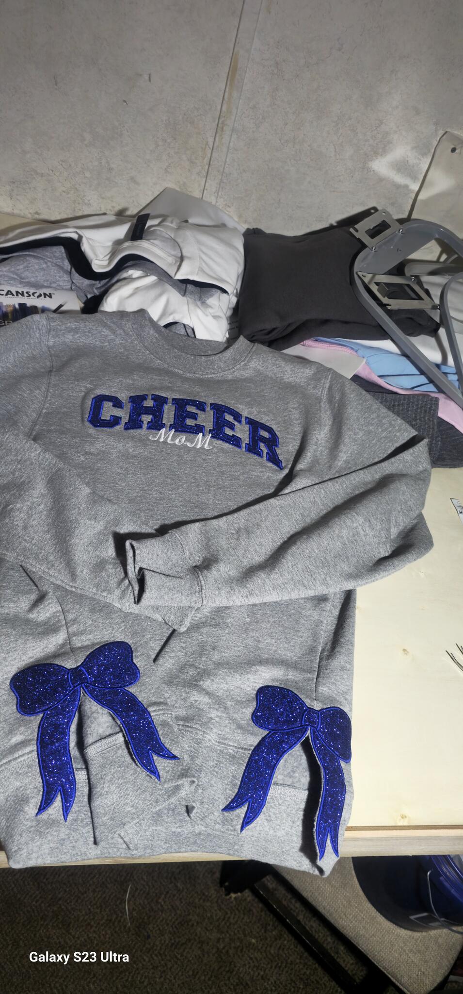 Gray CHEER MOM crewneck with blue glitter appliqué lettering and bows on both sleeves