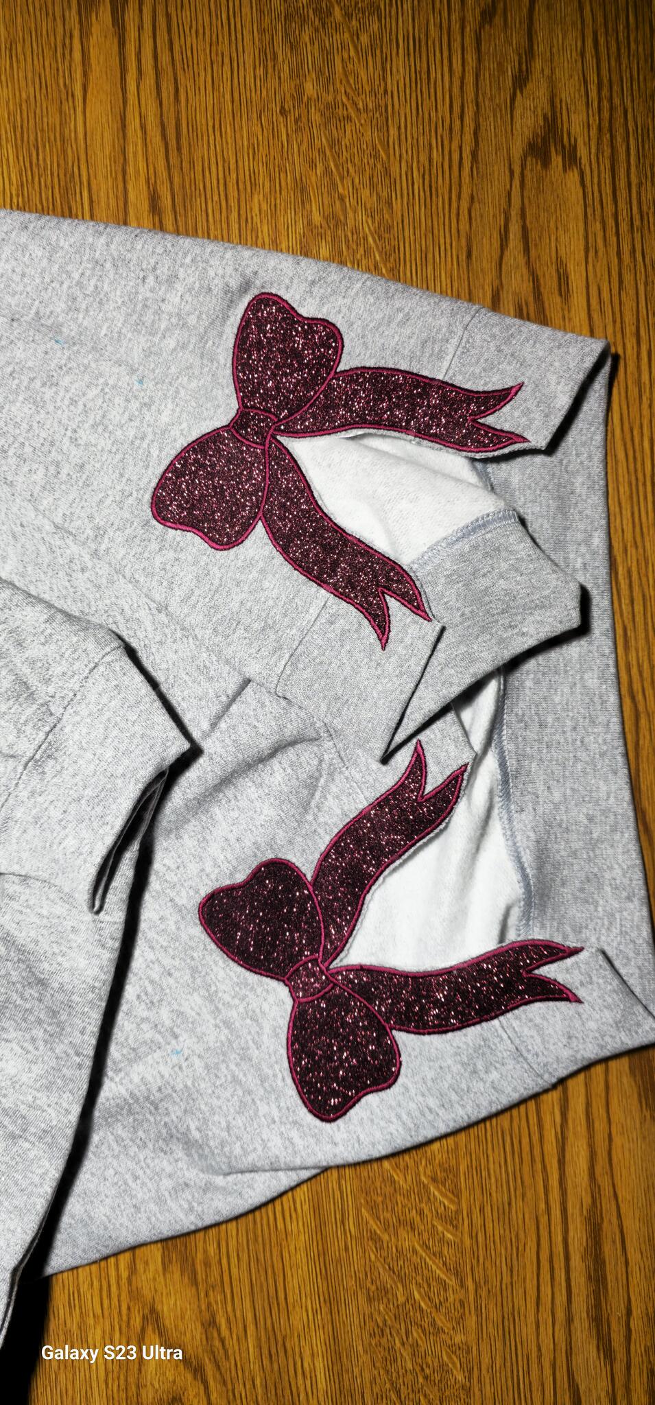Pink glitter bow appliqués with stitched edging on gray sleeves
