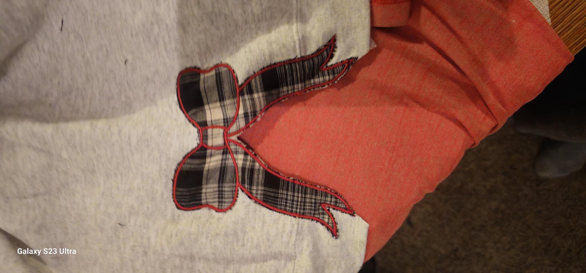 Black-and-white plaid bow appliqué edged in red stitching on gray fabric
