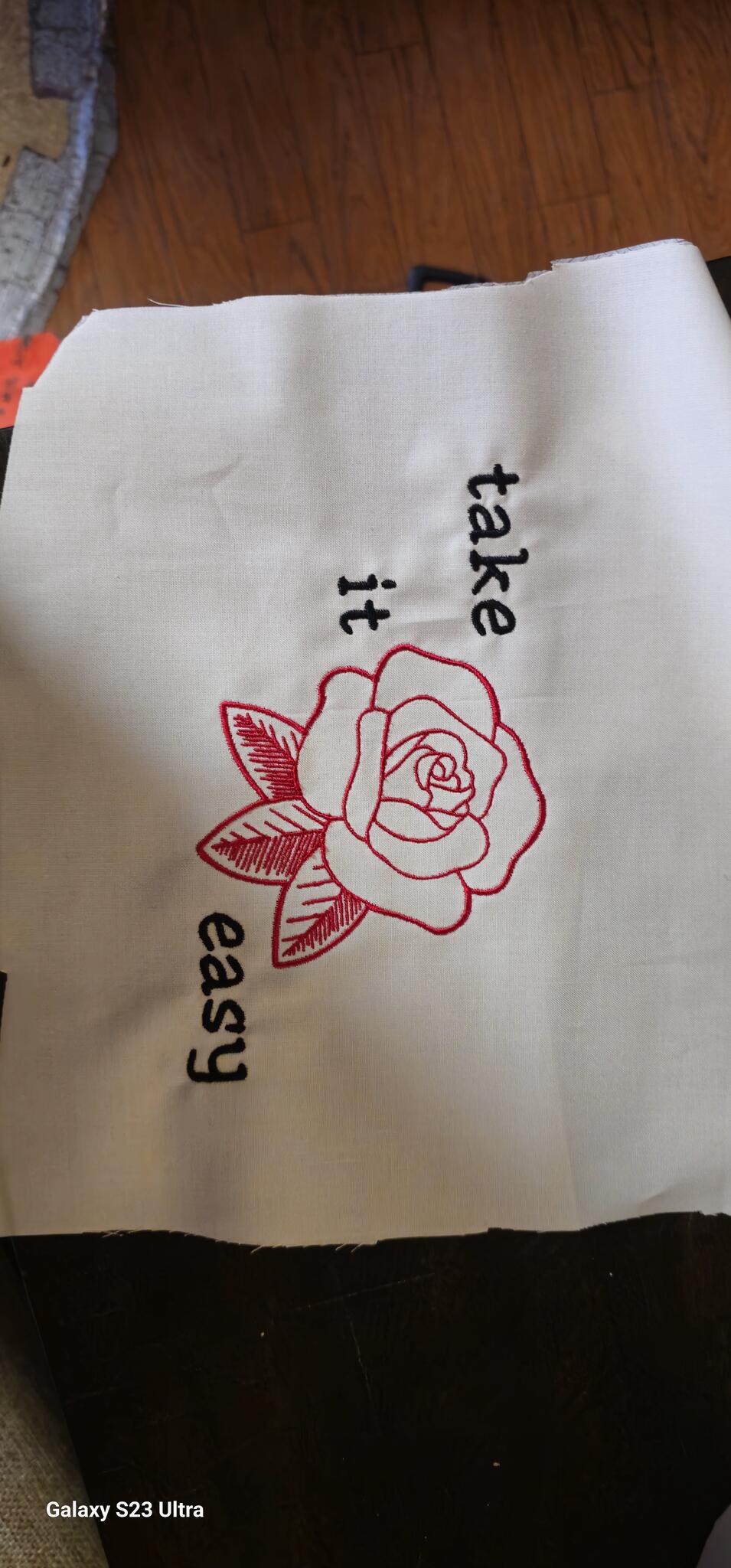 White fabric sample with a red outline rose and black take it easy lettering